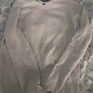 Beige stickad tröja - Mysig beige stickad tröja med rund halsringning och långa ärmar. Perfekt för kyligare dagar och enkel att matcha med olika outfits. Ribbstickade muddar vid ärmslut och nederkant ger en snygg detalj.