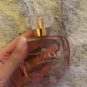Vive La Vie Eau de Parfum - En elegant parfymflaska i transparent rosa glas med guld- och kristalliknande kork. Doften är Eau de Parfum och flaskan rymmer 100 ml. Perfekt för dig som gillar feminina och fräscha dofter.