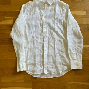 Vit linneskjorta från Skagen Clothing - Säljer en klassisk vit skjorta i linne från Skagen Clothing. Skjortan har lång ärm, knappar framtill och en avslappnad passform. Perfekt för varma dagar eller en stilren look. Snygg och enkel att matcha med det mesta!