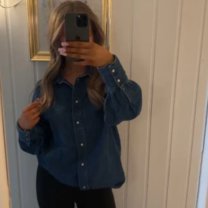 Blå jeansskjorta från Denim Rebel - Säljer en klassisk blå jeansskjorta från Denim Rebel. Skjortan har långa ärmar och knappar framtill. Perfekt för en avslappnad stil. Passar bra till både jeans och kjol. Går även att klä upp samt ha till vardags 