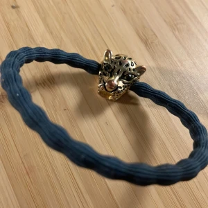 Elastiskt armband med leopardhuvud - Snyggt elastiskt armband med ett guldigt leopardhuvud som detalj. Armbandet har en mörkblå elastisk rem som ger en cool kontrast till det glänsande guldet. Perfekt för att lägga till en djärv touch till din outfit.