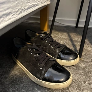 Lanvins - Snygga svarta sneakers från Lanvin med en unik design. Skorna har en kombination av mocka och lackdetaljer på tån, vilket ger dem en stilren look. Perfekta för dig som vill ha något extra i garderoben. Tveka inte på att skriva om du funderar över något. Nya skosnören följs med då dessa är smutsiga. (hjälper en vän)