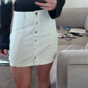 Vit kortkjol från Gina Tricot - Snygg vit kortkjol från Gina Tricot med knappar framtill. Kjolen har en normal passform. 