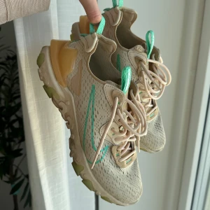 Beige sneakers med gröna detaljer - Snygga beige sneakers från Nike med gröna detaljer och snörning. Skorna har en unik design med perforerat mönster och en stabil sula. Perfekta för en sportig look.