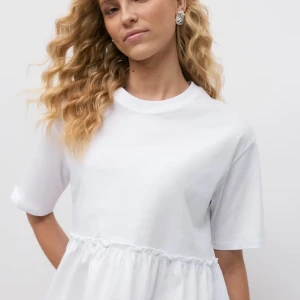 Vit blus med volangdetalj - Säljer en söt vit blus med volangdetalj i nederkant från gina, aldrig använd.  Blusen har korta ärmar och en rund halsringning. Perfekt för en stilren och avslappnad look.