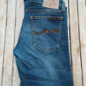 Blå jeans från Nudie Jeans - Snygga blå jeans från Nudie Jeans med klassisk femficksdesign och orange sömmar. Perfekta för en avslappnad stil. De har en knappgylf och en bekväm passform.