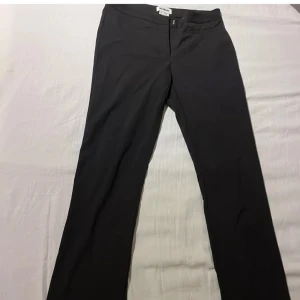 Svarta lågmidjade bootcut kostymbyxor  - Snygga svarta kostymbyxor från Weekday med låg midja och bootcut passform. Byxorna har en stilren design med dragkedja och knapp framtill. Perfekta för skola eller jobb nu till våren