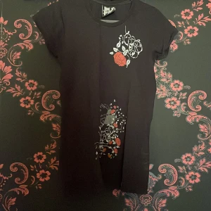 Svart t-shirt med tryck från Just A Fucking T-shirt - Säljer en svart t-shirt med coolt tryck av blommor och text i vitt och rött. Perfekt för dig som vill ha en unik stil. T-shirten är kortärmad och gjord i bomull. Passar perfekt till vardags eller när du vill sticka ut lite extra.