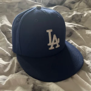 Blå LA keps från New Era - Säljer en blå LA keps från New Era. Perfekt för sportiga tillfällen eller som en stilren accessoar. Lätt böjd skärm. Storlek 6 7/8 (54,9cm) kepsen är köpt ifrån hatstore. Använd fåtal gånger.