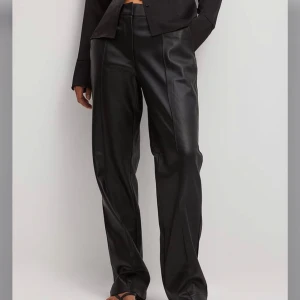 Svarta skinnbyxor - Snygga svarta skinnbyxor med hög midja och rak passform. Byxorna har en stilren design med diskreta fickor bak och en slät framsida. Perfekta för en trendig look.