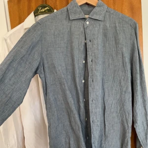 Blå linneskjorta - Snygg italiensk skjorta i linne med paramontura krage (handsydd i ett stycke) och handsydda pärlemo-knappar. Märket är Luca faloni och färgen heter french blue. Nypris: 2100kr (märket har aldrig reor). Storlek 39s, vilket motsvarar s-m slim fit. Fraktas mot betalning. 