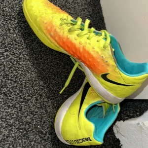 Gula och orange Nike fotbollsskor - Säljer ett par Nike fotbollsskor i en iögonfallande gul och orange färgkombination. Skorna har snörning och en svart Nike-logga på sidan. Perfekta för fotbollsplanen med sin sportiga design och bekväma passform.