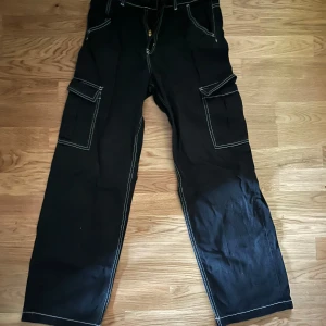 Svarta cargopants med vita sömmar - Snygga svarta cargopants med kontrasterande vita sömmar. Byxorna har flera praktiska fickor och en dragkedja framtill. Perfekta för en avslappnad stil.