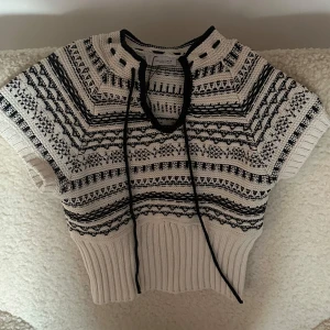 Svartvit stickad topp från Zara - Säljer en snygg svartvit stickad topp från Zara med korta ärmar och ett dekorativt snöre vid halsen. Toppen har ett detaljerat mönster och ribbad nederkant. Använt 1 gång. Den är i storlek s. Pris kan diskuteras 💕