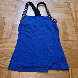 Blålila top med silverdetalj - Blålila top "Mindi" från Gina Tricot med rak skärning fram och svarta axelband som glimmar i silver. Tillverkad i mjuk viskosblandning med elastan för extra stretch. Skön och i mycket bra skick! Katt i hemmet. 