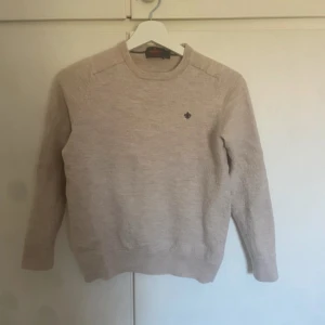 Beige tröja i merinoull från Morris - Säljer en stilren beige tröja från Morris i 100% merinoull. Tröjan har en liten broderad logga på bröstet och rund halsringning. Den passar någon som är 160-165