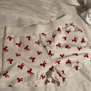 Vita boxershorts med röda rosetter - Säljer ett par vita boxershorts med ett mönster av röda rosetter. De har en bekväm resår i midjan. Perfekta för en avslappnad dag hemma.