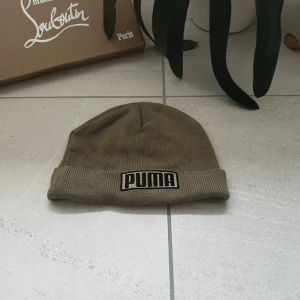 Olivgrön mössa från Puma - Snygg olivgrön mössa från Puma med broderad logga framtill. Tillverkad i mjukt och bekvämt material som håller dig varm under kyliga dagar. Perfekt accessoar för en sportig look. MVH EliteVolt