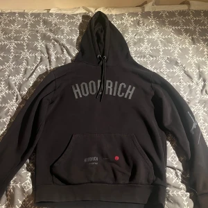 Svart hoodie från Hoodrich - Säljer en svart hoodie från Hoodrich med texten 'HOODRICH' på framsidan och 'FROM NOTHING TO SOMETHING' på baksidan. Hoodien har en stor ficka framtill och justerbar huva med snören. Det är en M men passar som en S med, 7/10 kvalitet.