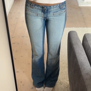 Blå jeans med broderi från Red Sky - Snygga blå jeans från Red Sky med unikt broderi på baksidan. De har en bootcut-stil och låg midja, vilket ger en avslappnad look. Jeansen har också röda sömdetaljer och en klassisk femficksdesign.