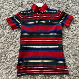 Randig pikétröja från Polo Ralph Lauren - Säljer en färgglad randig pikétröja från Polo Ralph Lauren. Tröjan har en klassisk krage med knappar och broderad logotyp på bröstet. Färgerna inkluderar röd, blå, grön och gul. Perfekt för en avslappnad stil. Hör av er vid minsta fråga och pris kan diskuteras! 