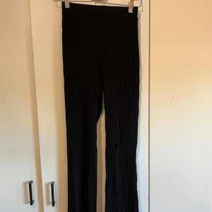Svarta ribbade byxor från Gina Tricot - Snygga svarta ribbade byxor från Gina Tricot. De har en hög midja och en bootcut-stil som ger en trendig look. Perfekta för att matcha med olika toppar och accessoarer.