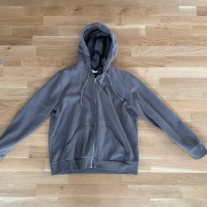 Brun hoodie med dragkedja - Säljer en stilren Brun hoodie med dragkedja och huva. Den har långa ärmar och ribbade muddar vid ärmslut. Perfekt för en avslappnad look.