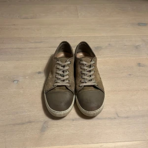 Lanvin - Snygga brun/begie sneakers från Lanvin i mocka med snörning och en vit sula. Perfekta för en stilren look. De har en rund tå och en diskret design som passar till många olika outfits. Skorna har en lite ”spricka”/slitage på tåboxen som syns lite på bilderna och vissa smutsfläckar men de lär gå bort med en simpel tvätt. Inget og följer med. Priset går och diskutera 