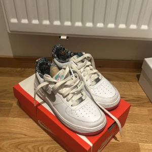 Nike Air Force 1 med färgglad detalj - Snygga Nike Air Force 1 sneakers i vitt skinn med silver swoosh och coolt färgglatt mönster på insidan. Skorna har klassisk snörning, perforerad tå och färgade detaljer på sulan. Perfekta för dig som vill sticka ut med en unik touch på dina sneakers. - Limited edition specials Nike air force.  Väldigt unika och knappt använda. Enkelt att tvätta dom. Köpte för 1900kr i London. Låda medföljer men INTE original låda