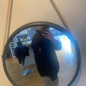 Svart vindjacka från Stone Island - Svart vindjacka från Stone Island med klassisk patch på vänster ärm. Jackan har dragkedja framtill och är tillverkad i lätt, meshfodrad polyester som andas. Perfekt för dig som vill ha en clean och stilren look med streetkänsla. Passar m/L, skick 9/10 äkta såklart och pris in diskuteras