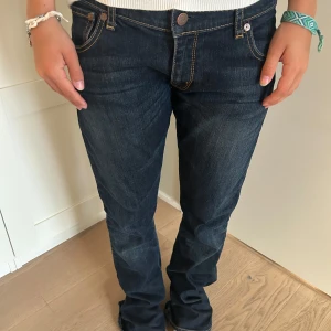 Mörkblå jeans från Stocker, rak modell - Säljer ett par mörkblå jeans från Stocker med klassisk rak passform och snygga kontrastsömmar. Jeansen har fem fickor, låg midja och coola detaljer på bakfickorna. Perfekta till sneakers eller boots för en avslappnad look.