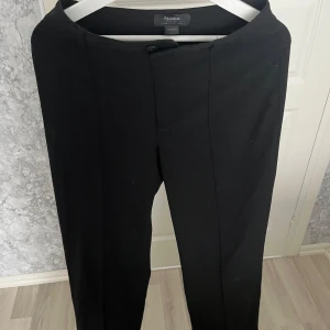 Svarta kostymbyxor från Pull&Bear - Svarta kostymbyxor från Pull&Bear med klassisk rak passform och pressveck längs benen. Byxorna har hög midja och stängs med knapp och dragkedja. Perfekta för en clean och stilren look. Materialet känns mjukt och följsamt. Vid frågor hör av dig!