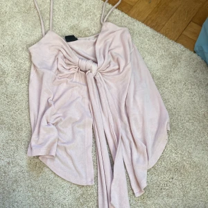 Ljusrosa linnetopp från Gina Tricot - Supersöt ljusrosa linnetopp från Gina Tricot med smala axelband och snygg knytdetalj framtill. Toppen har en flowy passform och är perfekt för varma dagar. Mjuk och lätt i materialet, vilket gör den riktigt skön att bära.