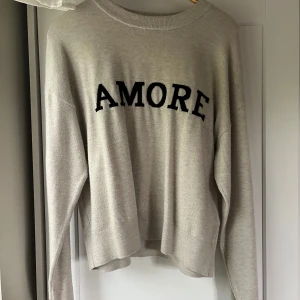 Beige stickad tröja med text från Gina Tricot - Beige stickad tröja från Gina Tricot med svart texten 'AMORE' framtill. Tröjan har en avslappnad passform, rund halsringning och långa armar💗 