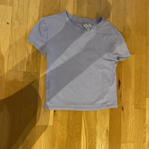 Ljuslila t-shirt från H&M Divided - En enkel och stilren ljuslila t-shirt från H&M Divided. Modellen är croppad med korta ärmar och rund halsringning. Perfekt att matcha med jeans eller kjol för en clean look.