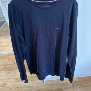 Svart långärmad tröja Tommy Hilfiger - Svart långärmad tröja från Tommy Hilfiger i ekologisk bomull. Klassisk rund halsringning, diskret logga på bröstet och stort Tommy Hilfiger-tryck längs ena ärmen. Perfekt basic med snygga detaljer för en stilren look. Använd fåtal gånger 
