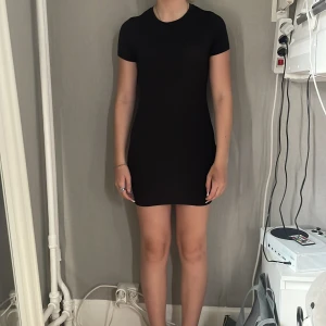 Svart tight kortklänning från Shein - Enkel och stilren svart kortklänning från Shein med tight passform. Klänningen har rund halsringning och korta ärmar, perfekt för en clean och minimalistisk look. Materialet är stretchigt och följsamt för en bekväm känsla.