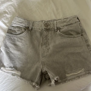 Grå jeansshorts från Zara - Snygga grå jeansshorts från Zara med råa kanter och slitningar framtill. Klassisk femficksmodell med bälteshällor och knappstängning. Perfekta för sommardagar när du vill ha en chill och trendig look.