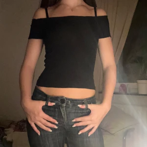 Svart croppad topp med ribbad struktur - Säljer en svart croppad topp med ribbad struktur och lätt vågad kant vid halsringningen. Toppen kan bäras både offshoulder och med vanliga axelband. Den är tight i passformen och har korta ärmar. Perfekt för dig som gillar en enkel men snygg stil.