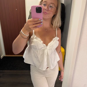 Vit poplin linnetopp med volang - Supersöt vit linnetopp i poplin med smala axelband, volangdetaljer vid bysten och liten knytning framtill. Luftig och flowy passform som är perfekt för varma dagar. Enkel att styla med både jeans och kjol.