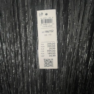 Glittrig silverklänning med volanger - Supersnygg glittrig klänning i silver med långa ärmar och flera volanglager. Klänningen har rund halsringning och smock i midjan för en markerad siluett. Perfekt för dig som vill sticka ut med metallic vibes och coola detaljer.