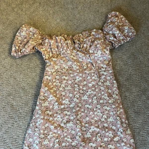 Blommig rosa kortklänning med puffärm - Supersöt kortklänning i ljusrosa med vitt blommönster och gröna blad. Klänningen har puffiga ärmar och en dragkedja i sidan som gör det lätt att sätta på sig den I storlek 34/xs🤍