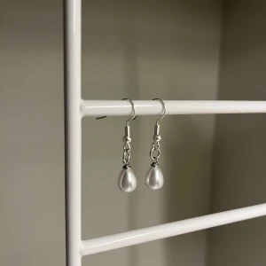Silvriga örhängen med pärldroppar - Rostfritt stål.Snygga örhängen med silvriga krokar och droppformade vita pärlor. Perfekta för att ge din look en elegant touch. Enkla att matcha med olika outfits och supertrendiga just nu.