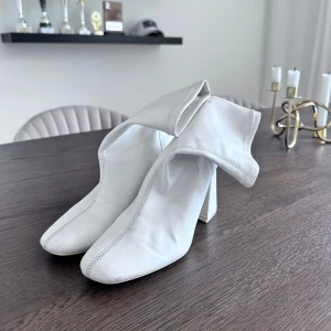 Vita stövletter med klack - Snygga vita stövletter med fyrkantig tå och bred klack. Skorna är i mjukt skinn och har en stilren, minimalistisk design som ger en modern vibe. Perfekta för dig som vill sticka ut med ett par trendiga boots i garderoben.