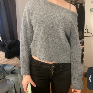 Grå offshoulder stickad tröja - Mysig grå stickad tröja med offshoulder-design och croppad passform. Tröjan har lång ärm och är supermjuk, perfekt till hösten. ifrån samsoe i storlek xs! den är i kashmir. 