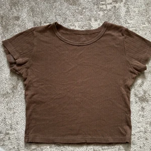 Brun ribbad kortärmad topp - Säljer en brun ribbad topp från Brandy Melville med korta ärmar och rund halsringning. Toppen har diskreta små hålmönster i rader och är croppad i modellen. Skriv vid frågor🩷🌟