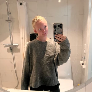 Grå stickad tröja från Zara - Mysig grå stickad tröja från Zara med rund halsringning och avslappnad passform. Tröjan har långa ärmar och ribbade muddar vid hals, ärmslut och nederkant. Perfekt för lager-på-lager under kyliga dagar.