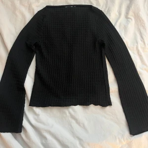 Svart långärmad topp lager 157 - Svart långärmad topp från lager 157 i storlek XS. Tröjan har ett vågigt, strukturerat mönster. Modellen har rak halsringning och sitter snyggt på kroppen. 