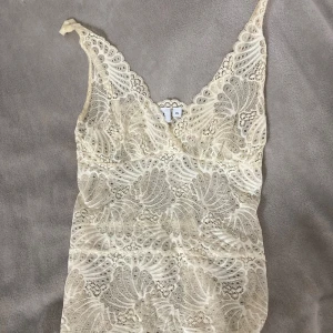 Spetslinne från Saint Tropez XS - Supersött linne i krämvit spets från Saint Tropez. Topp med smala axelband, v-ringning och detaljerat spetsmönster över hela plagget. Perfekt att styla lager på lager eller som den är för en romantisk vibe.