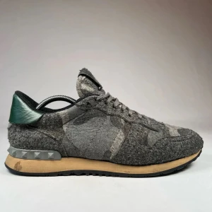 Valentino Garavani Rockrunner sneakers - Unika Valentino Rockrunner sneakers i grå ull med camouflagemönster och coola nitar på hälen. Skorna har snörning, beige sula och en mörkgrön detalj på hälen. Perfekta för dig som vill sticka ut med stil och streetkänsla.